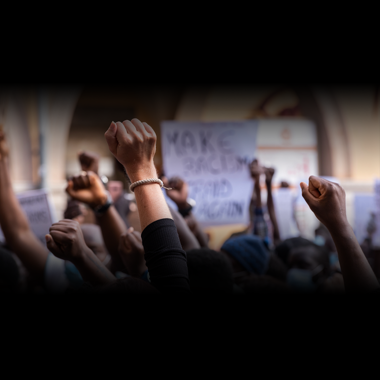 stock image of young people raising fists in the air with illegible signs of protest in the background