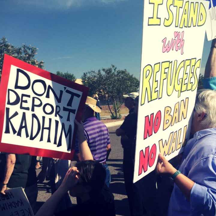 Protesters hold posters that read "Don't deport Kadhim" and "I stand with refugees.  No ban. No wall."
